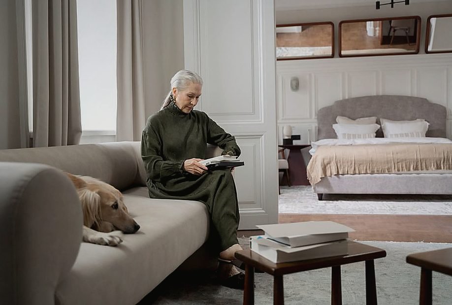 Senior woman in cozy living room reading a book with her pet dog by her side — legat de azil seniori Senior woman in cozy living room reading a book with her pet dog by her side — legat de azil seniori